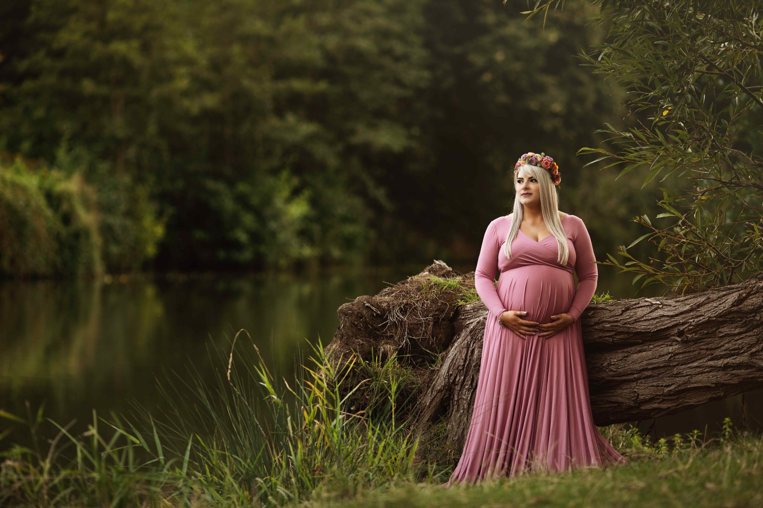 Pregnant woman in pink dress standing by a lake by Newborn Photographer in Medway, Kent