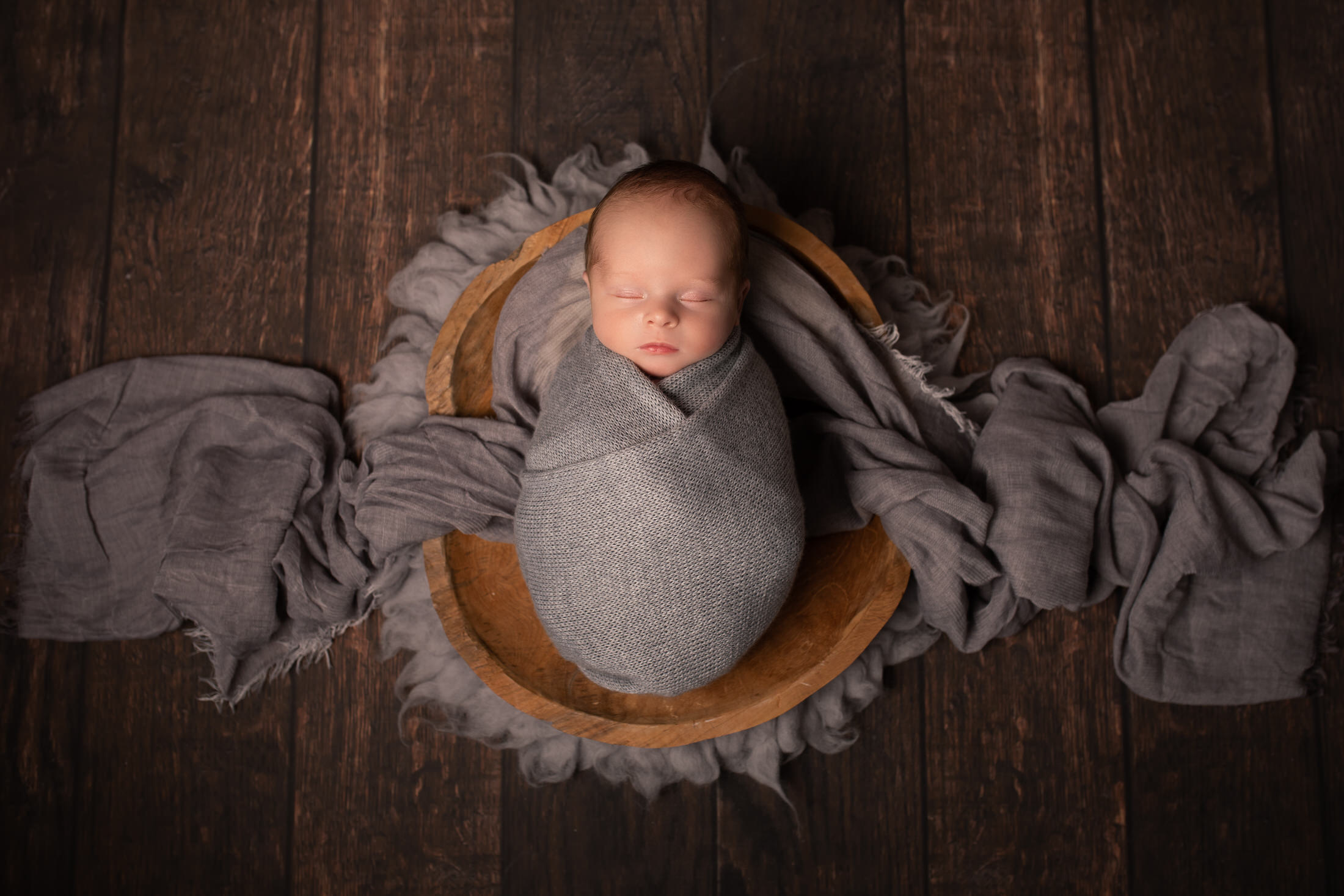 Baby boy with grey swaddling wrap in a wooden bowl by Newborn Photographer in Medway, Kent