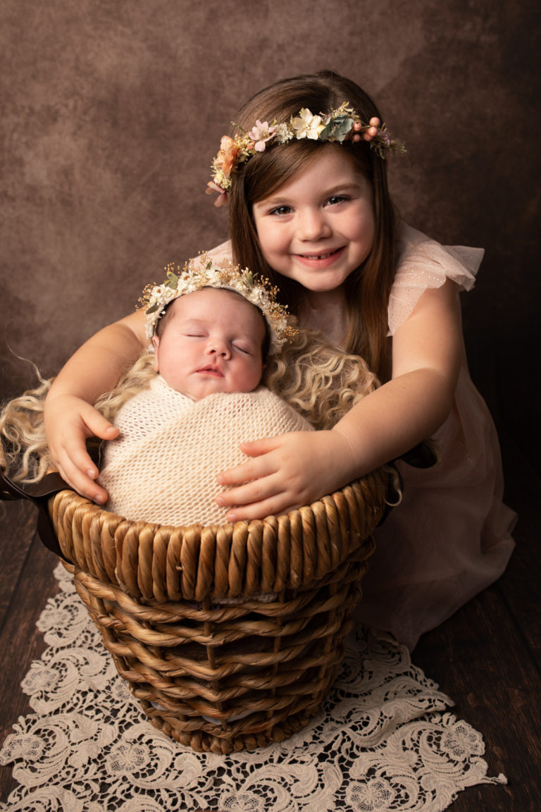 Sibling photo. Newborn wrapped in a cream blanket with older sister snuggling in. Photographed in Medway Kent