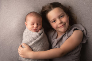 Sibling photo. Big sister holding newborn baby who is wrapped. Photographed by Hannah Cornford Photography in Strood