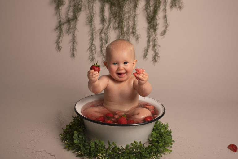 Fruit bath in Medway Kent. Baby girl sitting in a bowl with strawberries which she is enjoying eating