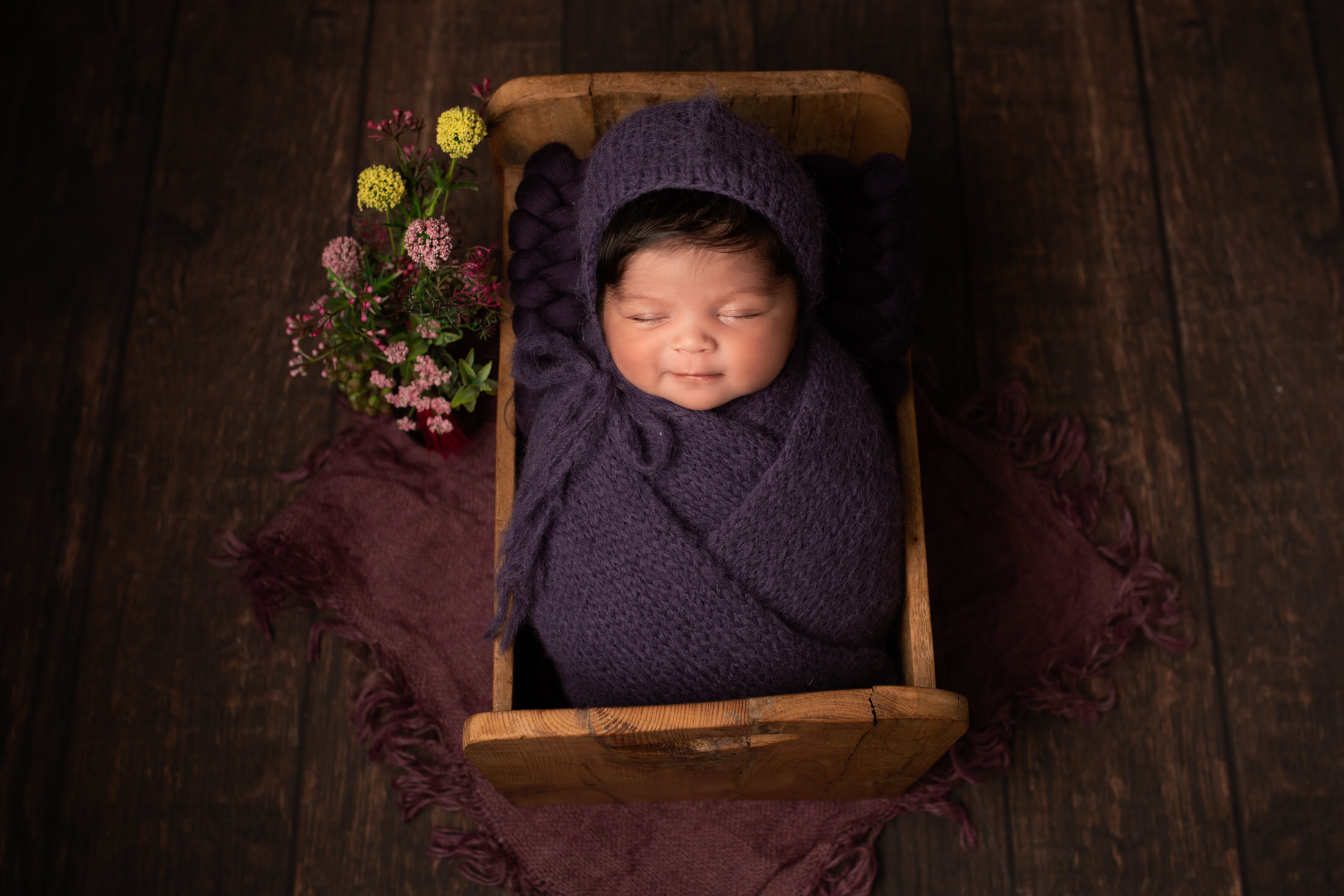 A baby girl wrapped in a dark purple wrap in a wooden bed by Newborn Photographer in Medway, Kent