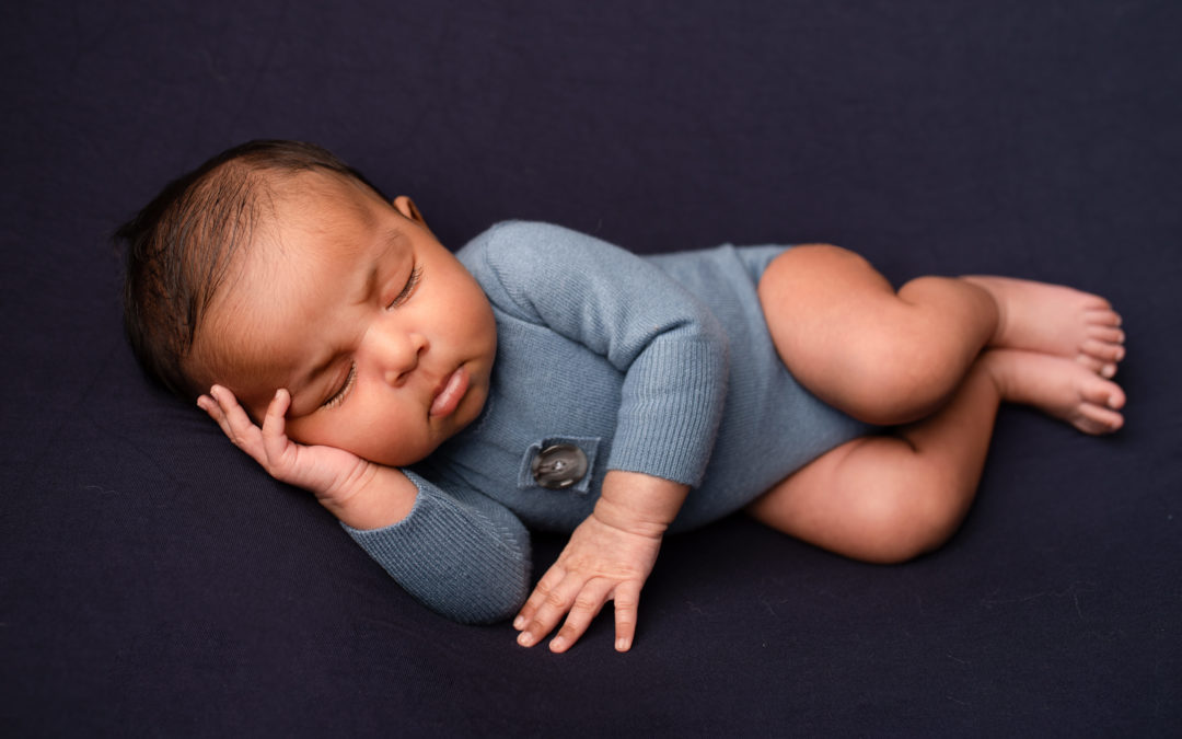 Newborn baby boy photographed in my studio in Strood, Medway Kent. The little boy is wearing a blue romper on a navy backdrop.