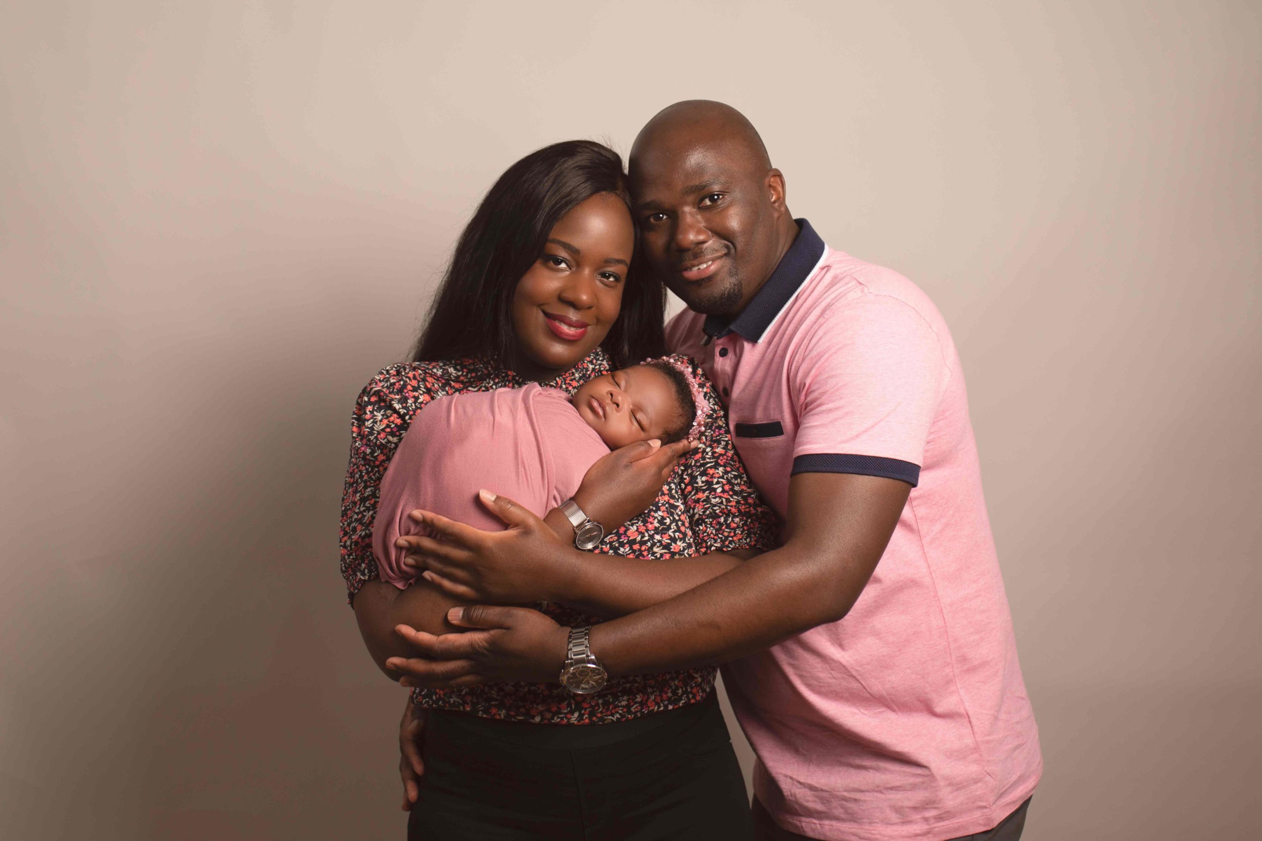 Parents holding newborn baby who is wrapped in pink by Newborn Photographer Medway