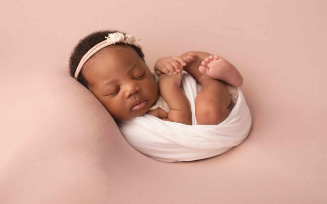 Newborn baby photographed in my studio based in Strood, Medway Kent. Baby is swaddled in a pink wrap with pink hairband
