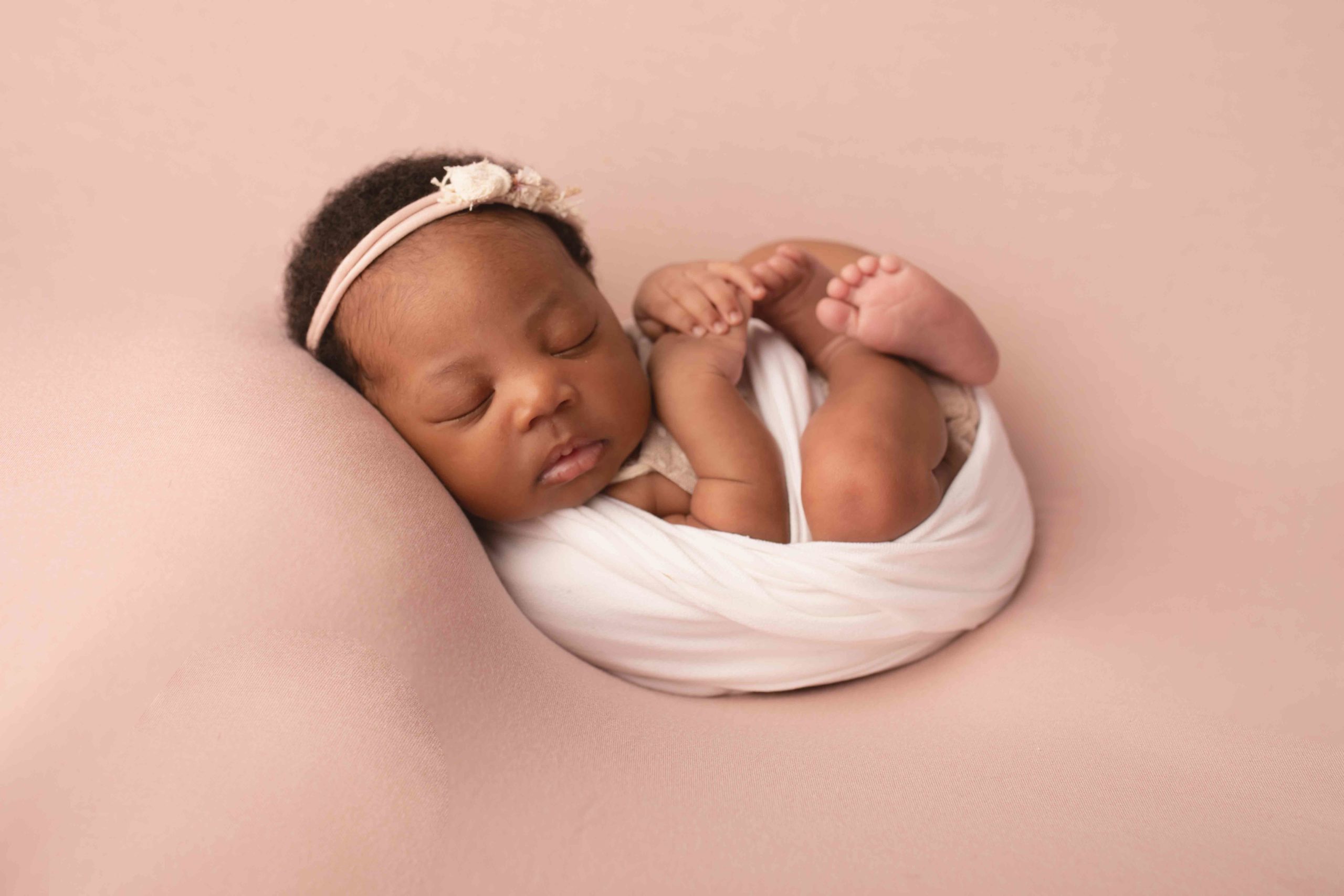 Baby girl wrapped in cream wearing cream headband on pink backdrop by newborn photographer in medway