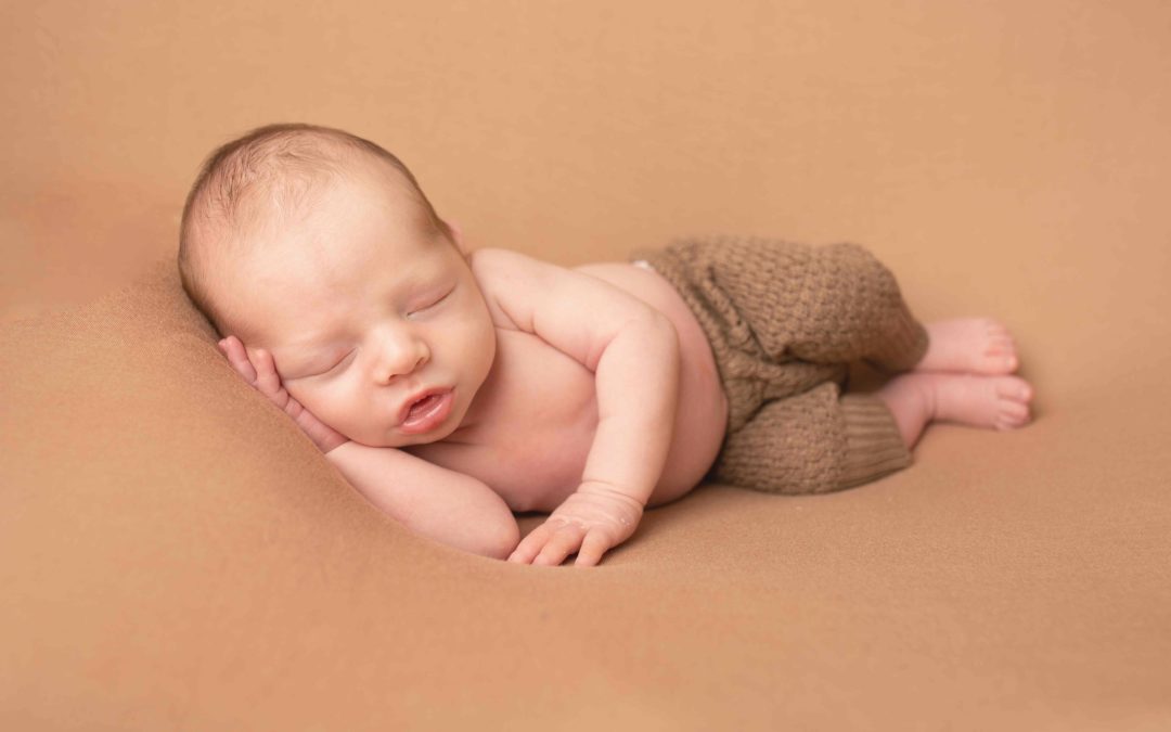 Baby boy wearing brown trousers laying on his side. Newborn baby Photographer Medway Kent