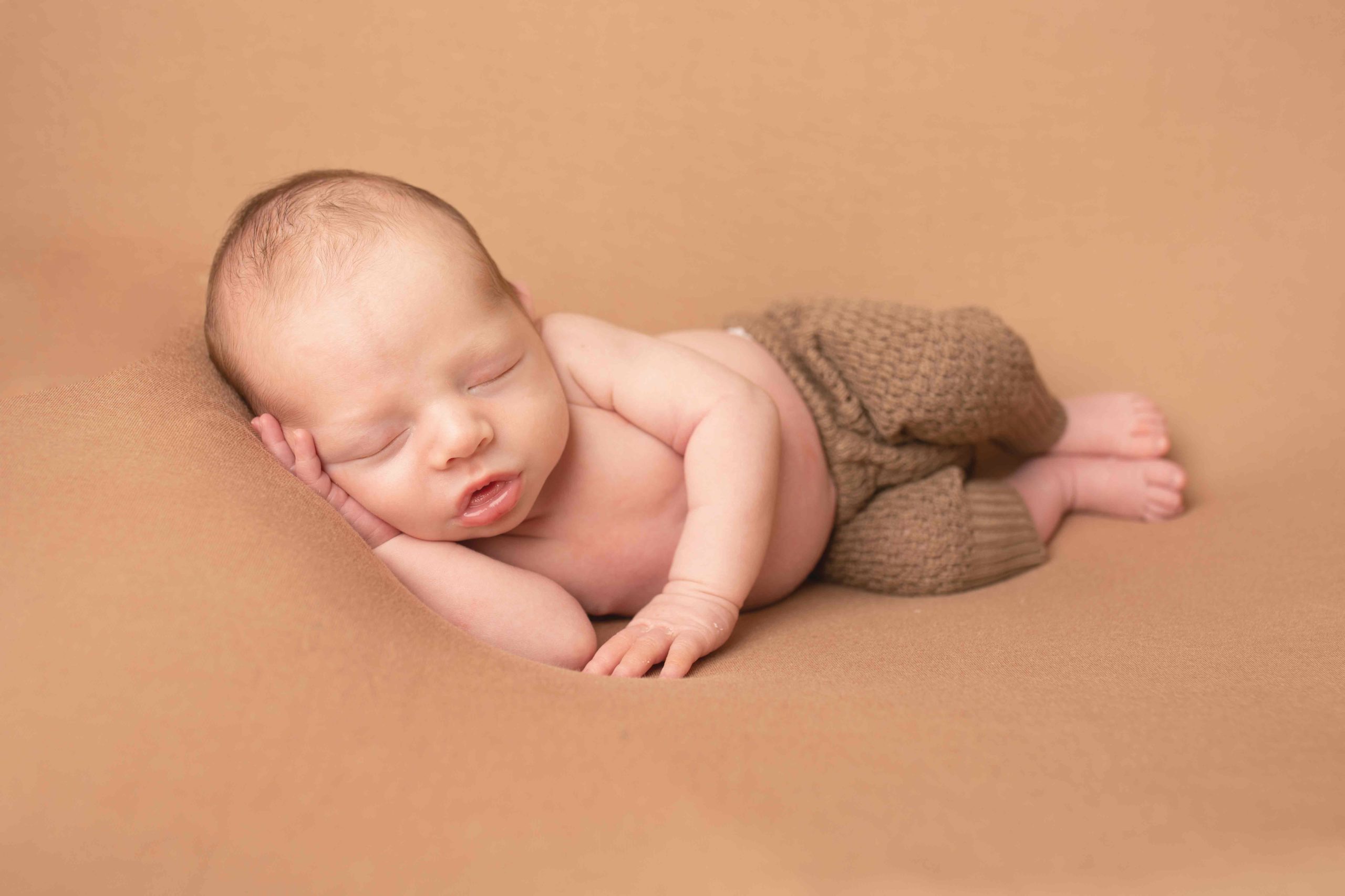 Baby boy wearing brown trousers laying on his side by Newborn Photographer Medway