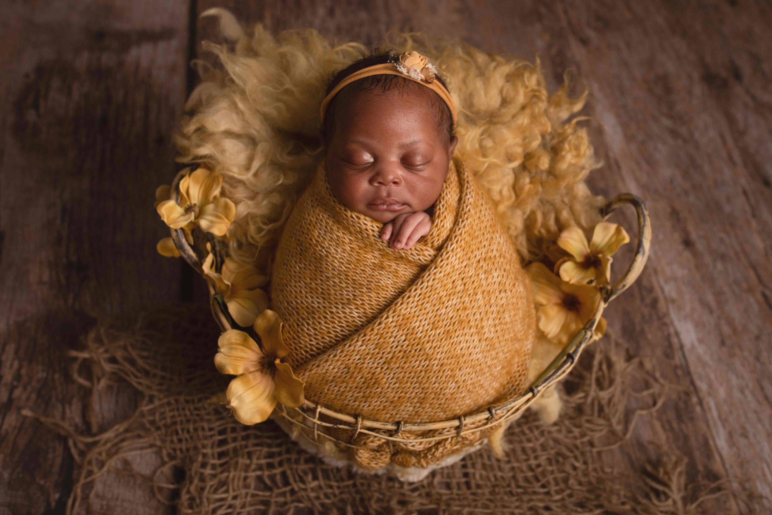 A yellow basket on wooden floor with newborn baby girl Newborn Photographer in Medway