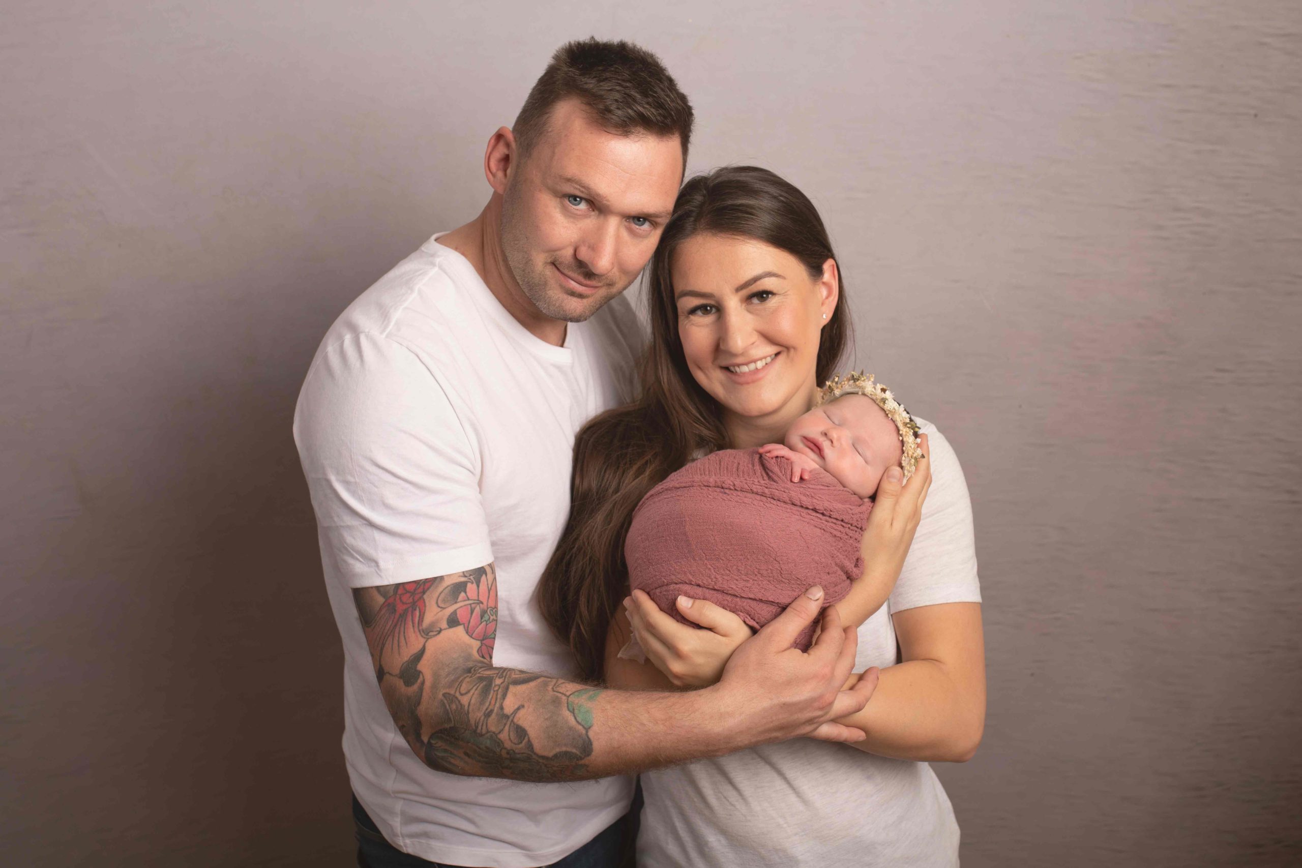 Mum, dad and baby girl wrapped in pink wrap all cuddled up by Newborn Photographer in Medway
