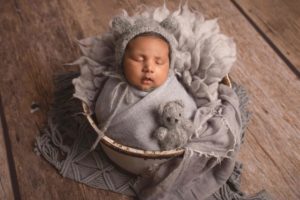 A wooden bucket with wrapped up newborn baby in grey with little teddy by Newborn Photographer in Medway , Kent
