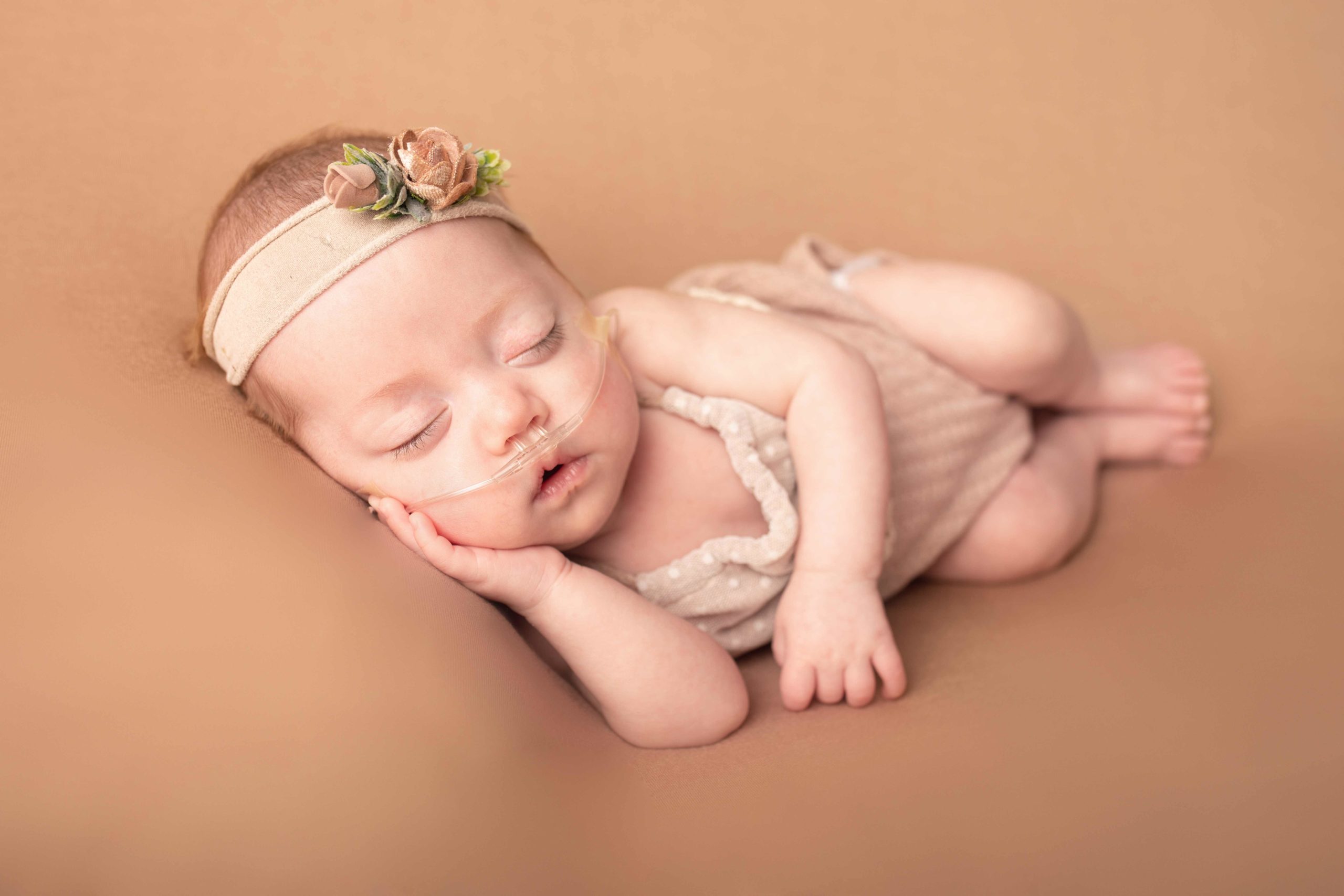 Newborn baby girl laying on her side with head in hand. Wearing cream romper by Newborn photographer in Medway