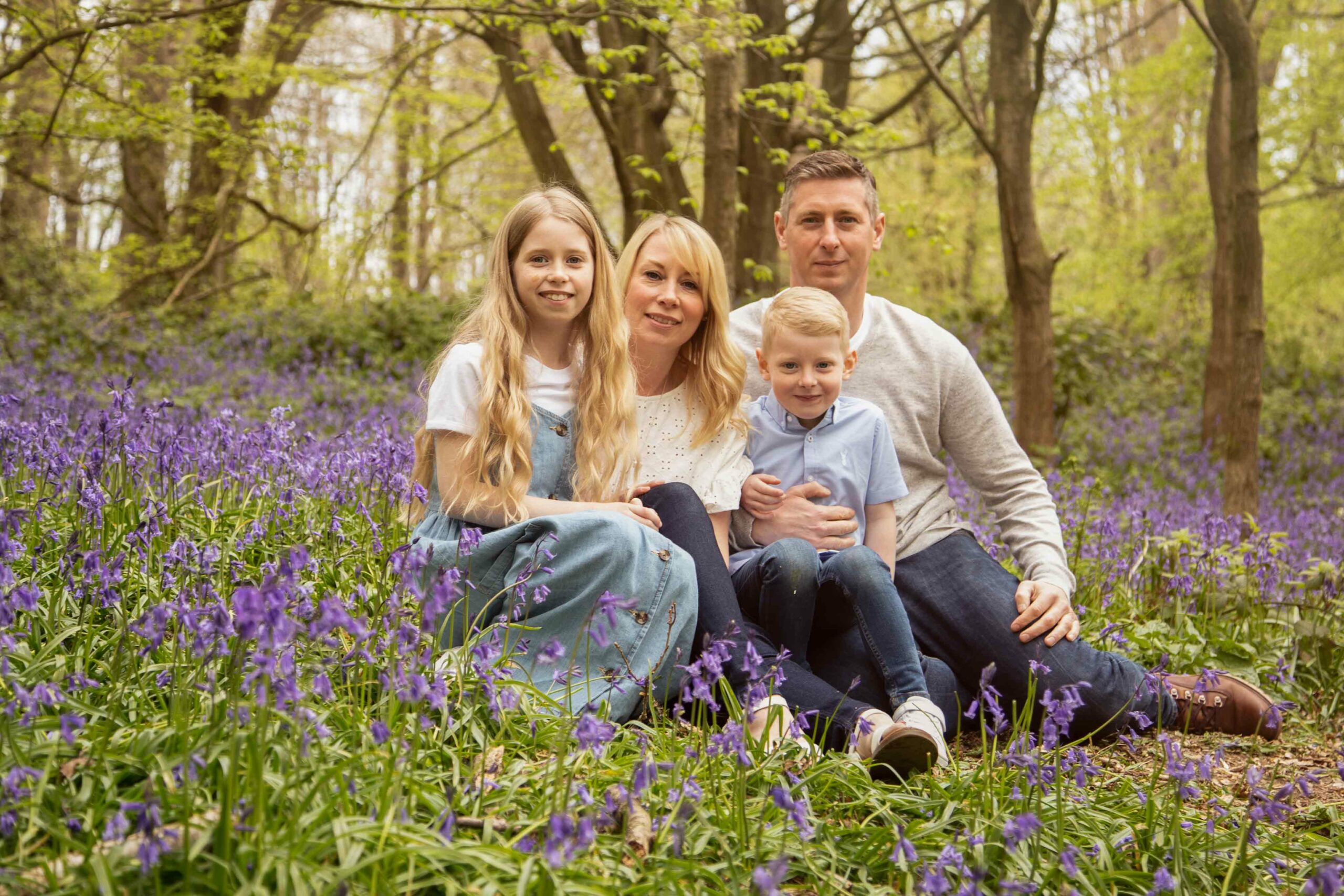 Family Photographer based in Medway, Kent. Photo of family sitting in bluebell covered woodland