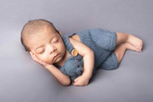 Newborn baby boy laying on blue blanket cuddling blue teddy. Photographed by Hannah Cornford Photography