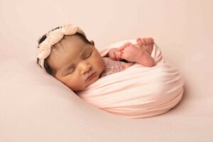 Newborn baby girl wrapped up in pink wrap wearing a pink headband. Photographed by me a newborn and family photographer in my studio in Strood, Medway Kent