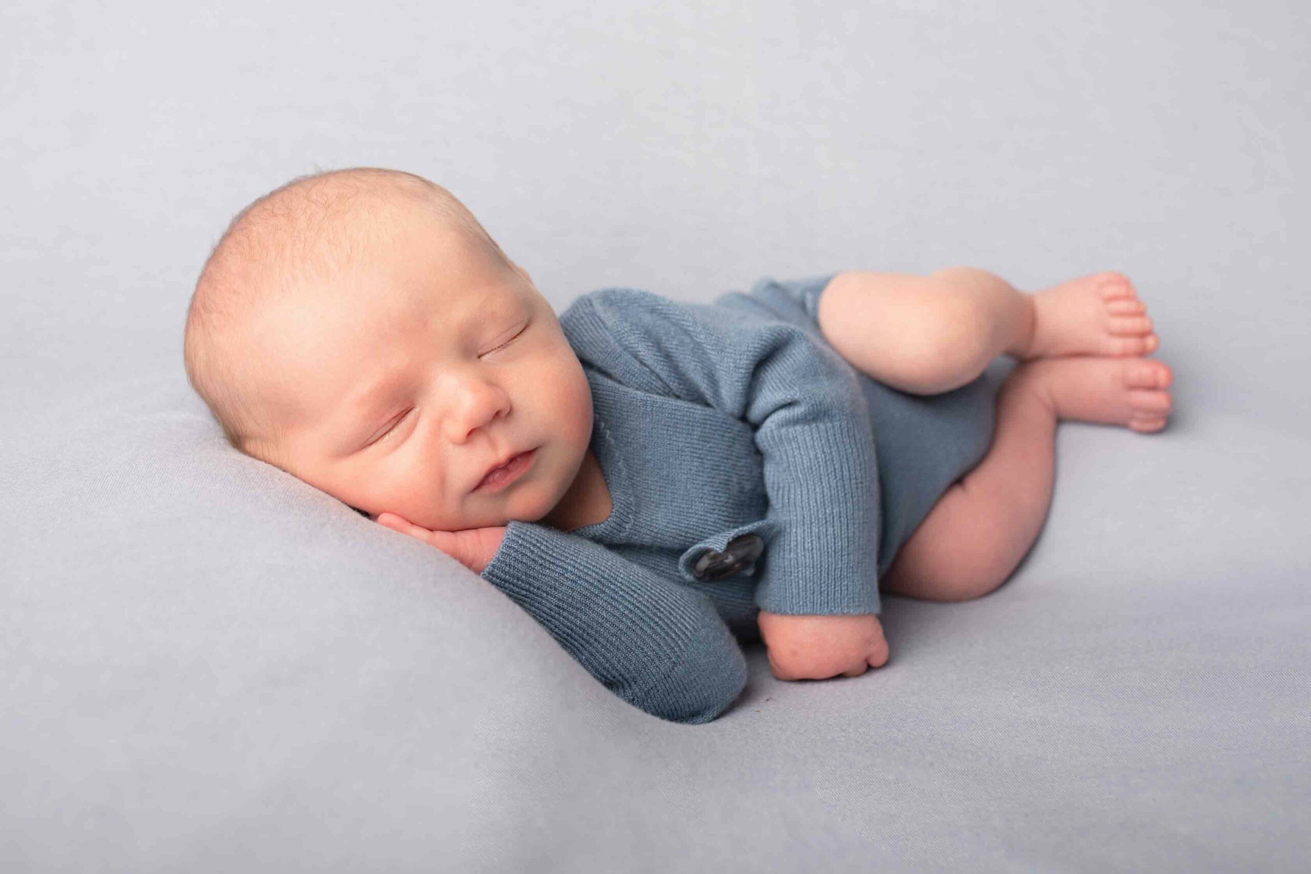 Newborn baby boy laying on blue background in blue outfit. Photographed in photo studio in Strood by Hannah Cornford