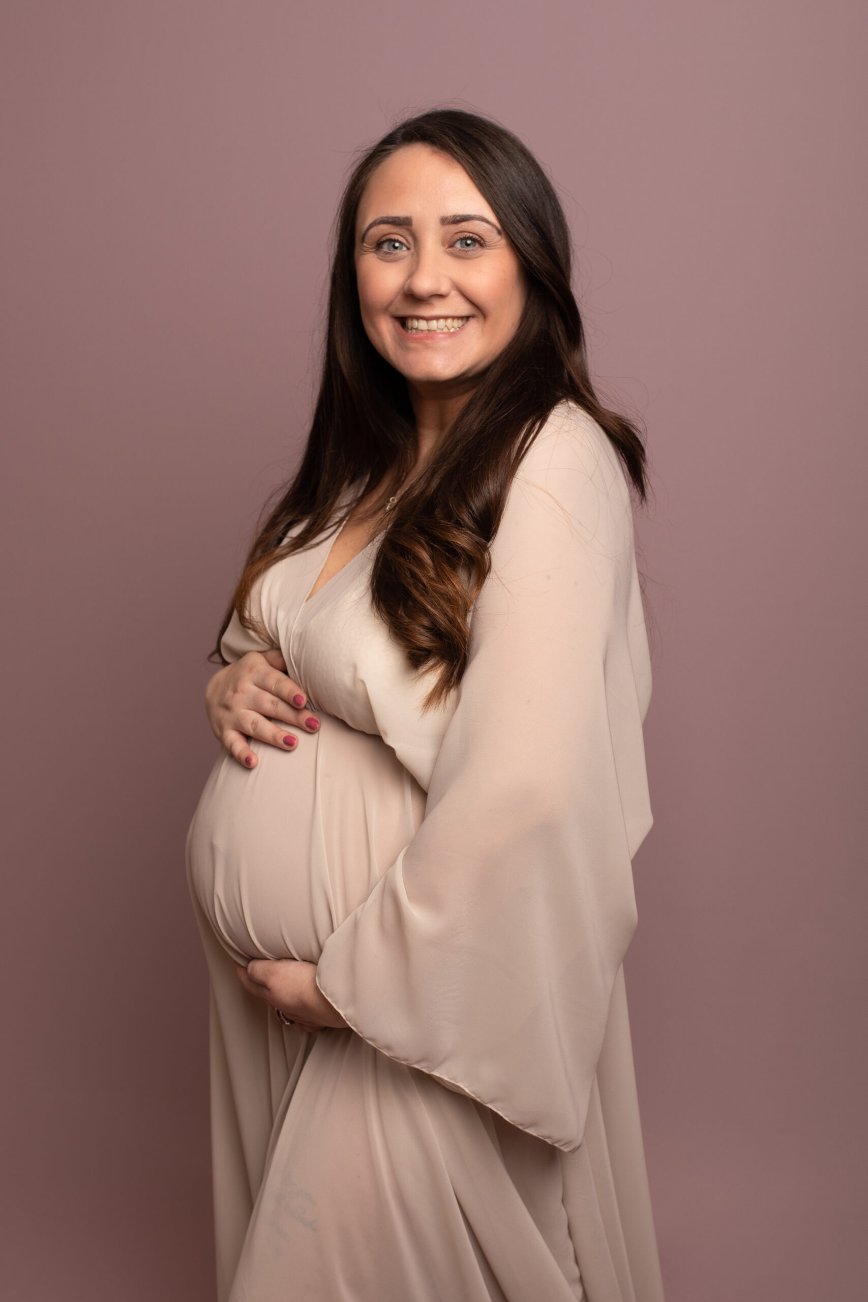 Pregnant mum to be wearing cream floaty dress on a pink background. Photographed in Kent studio by Hannah Cornford Photography