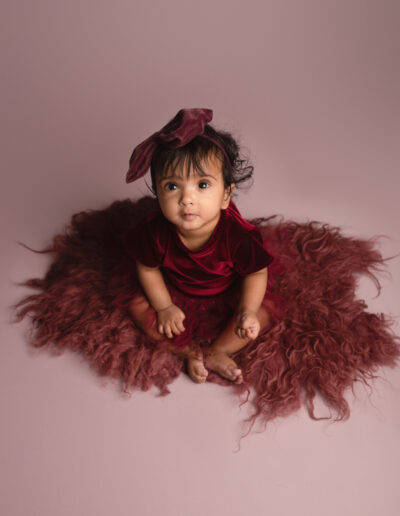 Baby girl dressed in red tutu dress sitting on pink backdrop photographed by Hannah Cornford in Medway, Kent.