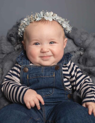 Baby girl wearing blue dungarees with a floral headband.Taken by Hannah Cornford Photography a Family and Newborn photographer based in Medway, Kent.