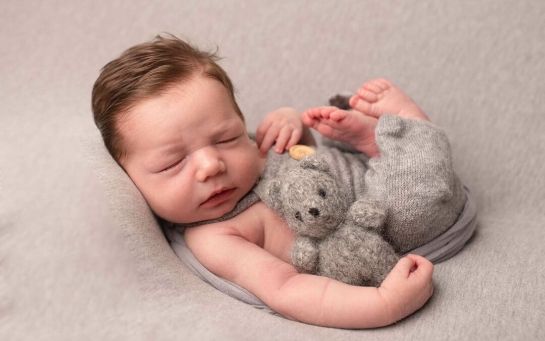 Baby boy wearing grey dungarees is cuddling a small grey teddy bear. Photographed by Hannah Cornford Photography in Medway Kent