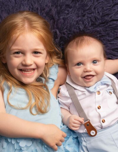 Two siblings a boy and a girl. The girl is older and is cuddling the boy. Both wearing blue outfits. Taken by Hannah Cornford Photography a Family and Newborn photographer based in Medway, Kent.
