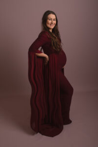 Pregnant lady wearing stunning burgandy red flattering gown. Photographed by Hannah Cornford photography in medway studio on pink backdrop.
