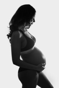 Maternity photo of a pregnant lady holding her bump with light coming from behind. Creating a beautifully lit silhouette