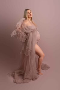Pregnancy photo with mum to be wearing dusky pink body suit with tulle gown over. Photographed on pink backdrop by Hannah Cornford in Medway Kent