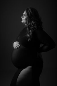 Beautiful pregnant lady wearing black dress holding her bump. Lit very lightly to just illuminate the bump and skin. Maternity Photo taken by Hannah Cornford Photography a Family and Newborn photographer based in Medway, Kent.